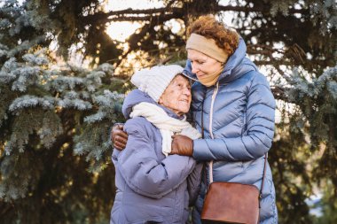Mutlu aile kavramı, yaşlılık, duygular, emeklilik yaşında yaşlı bakım. Aktif kıdemli büyükanne ve yetişkin kız kışın ormanda Noel ağacının arka planına sarılıyorlar..