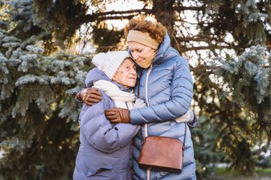 Mutlu aile kavramı, yaşlılık, duygular, emeklilik yaşında yaşlı bakım. Aktif kıdemli büyükanne ve yetişkin kız kışın ormanda Noel ağacının arka planına sarılıyorlar..
