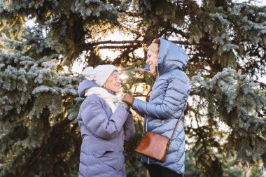Annelik. Temanın önemi, bayramlarda yaşlı bekar ebeveynleri ziyaret etmek ve onlarla vakit geçirmek. Büyük anne ve yetişkin kız mutlu aile kucaklaşması ve gülüşmeler Park arka planında kışın Noel ağacı.