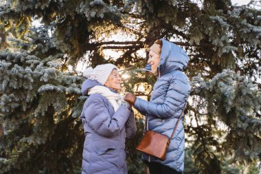 Beyaz kadınlar, kışın arka planda kışın anne ve kız çocuğu. Köknar ağacı, yüz yüze sarılırlar, gülümserler, yaşlı anne ve babalarla vakit geçirirler. Noel için ormanda yaşlı bir anneyle yürürler.