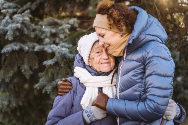 Annelik. Temanın önemi, bayramlarda yaşlı bekar ebeveynleri ziyaret etmek ve onlarla vakit geçirmek. Büyük anne ve yetişkin kız mutlu aile kucaklaşması ve gülüşmeler Park arka planında kışın Noel ağacı.