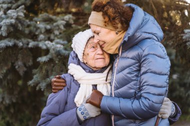 Beyaz kadınlar, kışın arka planda kışın anne ve kız çocuğu. Köknar ağacı, yüz yüze sarılırlar, gülümserler, yaşlı anne ve babalarla vakit geçirirler. Noel için ormanda yaşlı bir anneyle yürürler.