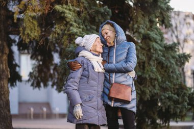 Annelik. Temanın önemi, bayramlarda yaşlı bekar ebeveynleri ziyaret etmek ve onlarla vakit geçirmek. Büyük anne ve yetişkin kız mutlu aile kucaklaşması ve gülüşmeler Park arka planında kışın Noel ağacı.