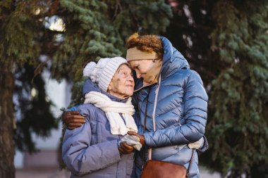 Annelik. Temanın önemi, bayramlarda yaşlı bekar ebeveynleri ziyaret etmek ve onlarla vakit geçirmek. Büyük anne ve yetişkin kız mutlu aile kucaklaşması ve gülüşmeler Park arka planında kışın Noel ağacı.