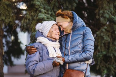 Mutlu aile kavramı, yaşlılık, duygular, emeklilik yaşında yaşlı bakım. Aktif kıdemli büyükanne ve yetişkin kız kışın ormanda Noel ağacının arka planına sarılıyorlar..