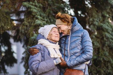 Annelik. Temanın önemi, bayramlarda yaşlı bekar ebeveynleri ziyaret etmek ve onlarla vakit geçirmek. Büyük anne ve yetişkin kız mutlu aile kucaklaşması ve gülüşmeler Park arka planında kışın Noel ağacı.