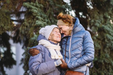 Mutlu aile kavramı, yaşlılık, duygular, emeklilik yaşında yaşlı bakım. Aktif kıdemli büyükanne ve yetişkin kız kışın ormanda Noel ağacının arka planına sarılıyorlar..