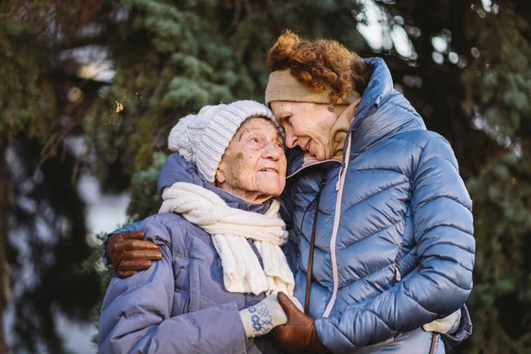 Motherhood. Theme importance visiting and spending time with old single parents during holidays. Senior mom and mature daughter happy family hug and laugh in park background Christmas tree in winter.