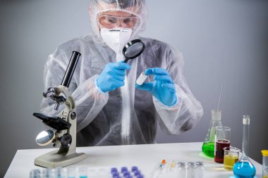 Büyüteci olan bir bilim adamı. Covid-19 ve aşı arayışı, kimyager tıp laboratuarındaki büyüteçler vasıtasıyla koronavirüs aşısı şişesini inceliyor. Test, bağışıklık sistemi, enjeksiyon.