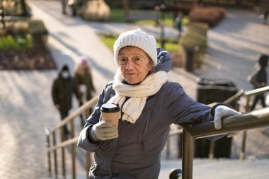 Şehirdeki hoş, son sınıf öğrencisi kadın kışlık ceketiyle, şapkasıyla, atkıyla ve güneşli kış havasında eldiven örerek kahve içiyor. Yanında bir fincan sabah kahvesi götüren yakışıklı bir kadın..