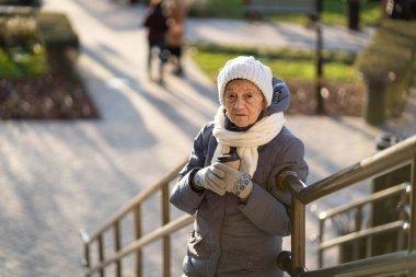 Elinde kahve tutan neşeli yaşlı bayan, şehirde kışlık kıyafetler giyiyor. Kahveli güzel yaşlı bayan. Yaşlılıkta aktif dinlenme, yürüyüş sırasında kahve molası. Sıcak içecek, 90 yıl emekli..
