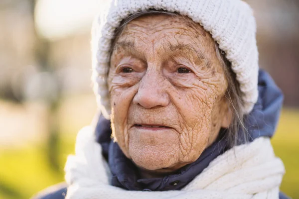 Outdoor portrait of senior woman in jacket , scarf and head wear in winter. Happy retirement. Joyful elderly person posing in park, sunny cold weather. Happy mature woman enjoying walk in town.
