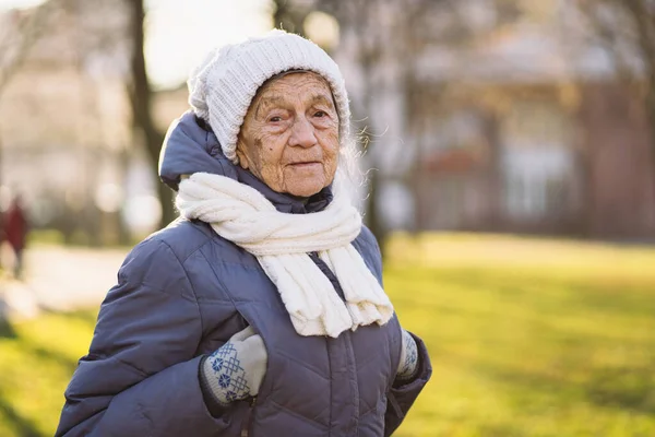 白种人老年妇女 头发灰白 皱纹很深 90岁 穿着保暖衣服 公园里戴着白色针织围巾和帽子 阳光灿烂 天气寒冷 活跃的老年妇女 行走的老年妇女 — 图库照片