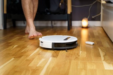 Ev işleri ve teknoloji konsepti. Robot elektrik süpürgesinin bakımı ve bakımı. Temizlik, onarım, yedek parça. Evde robot temizleyiciyi tamir eden adam. Akıllı ev fonksiyonları, tam otomatik.