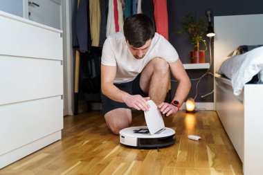 Robot elektrik süpürgesi tamiri. Robot elektrik süpürgesini tamir eden adam evde yerde yatıyor. Robotik elektrik süpürgesi bakım ve servisi. Kolay ev işleri için akıllı bir alet. Haneler için yeni teknoloji.