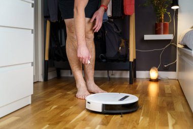 Kafkasyalı genç adam beyaz robot elektrik süpürgesi bakımı yapıyor. Özerk kablosuz modern elektrikli süpürge. Erkek, yerde robot temizleyici tamir ediyor. Elektrikli süpürge robot tamir konsepti.