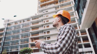 İnşaat alanındaki girişimciler akıllı telefon kullanır, iş planlarını kontrol ederler. İnşaat mühendisi ya da mimar. Akıllı telefonda sabit kasklı kontrol programı var. Mühendis bina projesini kontrol ediyor..