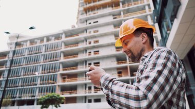 İnşaat alanındaki girişimciler akıllı telefon kullanır, iş planlarını kontrol ederler. İnşaat mühendisi ya da mimar. Akıllı telefonda sabit kasklı kontrol programı var. Mühendis bina projesini kontrol ediyor..