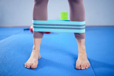 Spor giyim kuşağında çıplak ayaklı atletik bir kadın esnek kumaş egzersiz bantlarını spor salonu için bant, ağırlık kaldırma, antrenman kasları için kullanıyor. Sıska kız iyi durumda..