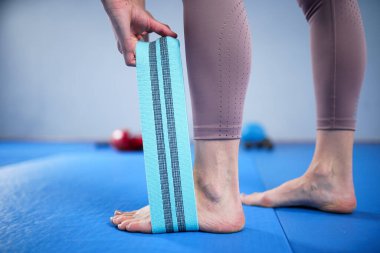 Spor giyim kuşağında çıplak ayaklı atletik bir kadın esnek kumaş egzersiz bantlarını spor salonu için bant, ağırlık kaldırma, antrenman kasları için kullanıyor. Sıska kız iyi durumda..