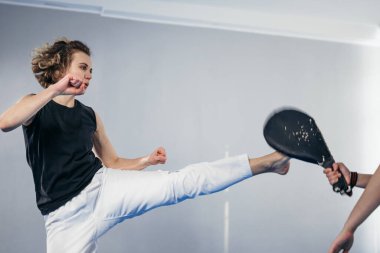 Antrenörle antrenman yapan kadın dövüş sanatları dövüşçüsü tekvando tekmesi egzersizi yapıyor. Kickboksçu kadının çıplak ayakla vurması, kum torbasını yumruklaması, kalkanı tekmelemesi..