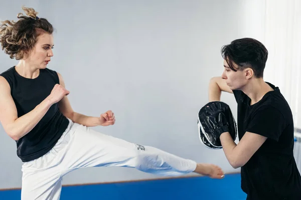 Female martial arts fighter practicing with trainer, punching taekwondo kick pad exercise kicking. Training of kickboxer woman strikes with bare foot mitts punching bag kicking shield.