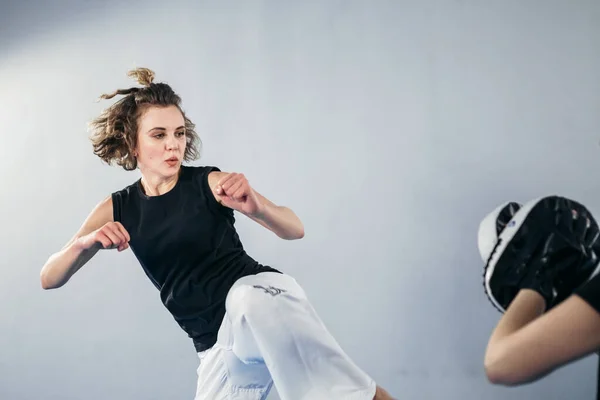 Female martial arts fighter practicing with trainer, punching taekwondo kick pad exercise kicking. Training of kickboxer woman strikes with bare foot mitts punching bag kicking shield.