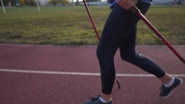 Sağlıklı yaşam tarzı kavramı. Olgun, beyaz bir kadın sopayla kardiyo egzersizi yapıyor ya da şehirdeki stadyum yolunda yürüyor. Yaşlıların etkinliği. Yaşlı kadın bastonla yürüyor.