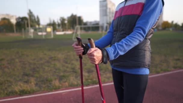 在体育场进行高年级女子步行杆训练。成熟的女性在跑道上做北欧式的步行练习.健康的生活方式概念。在城镇里用手杖进行积极的女性运动 — 图库视频影像