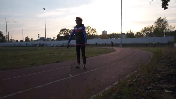 Mujer caucásica madura delgada haciendo ejercicios de fortalecimiento para calentar los músculos antes de que la caña nórdica caminar en el estadio de la ciudad. Mujer mayor haciendo ejercicio con palo. Actividades al aire libre. Caminata nórdica — Vídeos de Stock