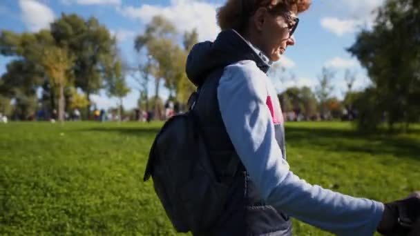 Idős nő sétál a parkban skandináv botokkal és kutya tacskóval. Boldog idős nő sétál a túrázó póznákkal. Senior hölgy nordic séta a városi parkban, napos időjárás kutyus — Stock videók