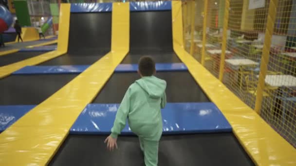 Felice sorridente 11 anni i bambini che saltano sul trampolino all'interno nel centro di intrattenimento. Bambini attivi tempo libero, saltare e giocare sul trampolino nel centro sportivo. Parco divertimenti. Attività sportive — Video Stock