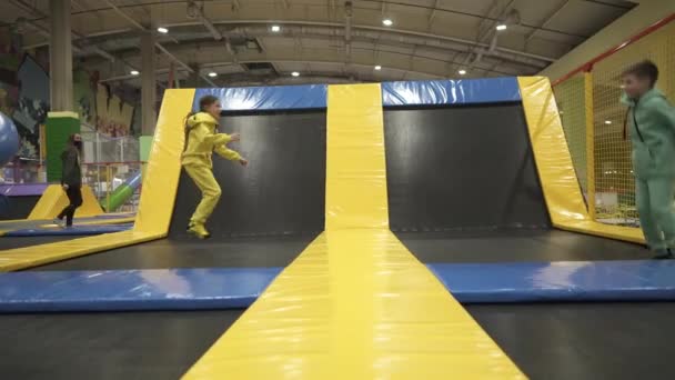 Feliz sonrisa 11 años de edad, los niños saltando en el trampolín interior en el centro de entretenimiento. Niños activos de ocio, saltando y jugando en trampolín en el centro deportivo. Parque de atracciones. Actividad deportiva — Vídeos de Stock