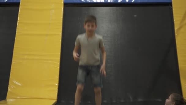 Glada leende 11 år gamla barn hoppar på studsmatta inomhus i nöjescentret. Aktiva barn fritid, hoppa och spela på studsmatta i sportcenter. Nöjespark. Idrottsverksamhet — Stockvideo