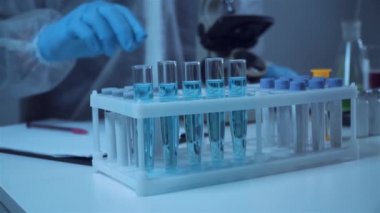 Mavi lateks eldivenleri teslim eden bilim adamlarının yakın çekimleri laboratuardaki deney tüpündeki kimyasal sıvıyı inceliyor. Araştırma ve geliştirme. Laboratuvar teknisyeni deneysel bir maddeyi inceliyor.