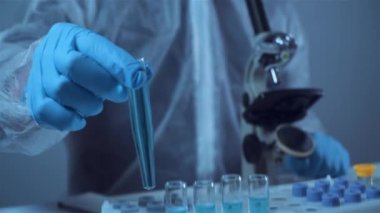 Koruyucu tulum giyen bilim adamı ya da doktor mavi reaktörlü test tüpü, kimyasal sıvı, mikroskop, laboratuvar biyokimyası içeren laboratuvar camları alıyor. Tıp ve araştırma konsepti