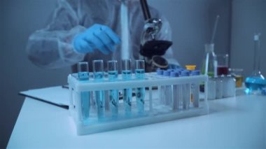 Mavi lateks eldivenleri teslim eden bilim adamlarının yakın çekimleri laboratuardaki deney tüpündeki kimyasal sıvıyı inceliyor. Araştırma ve geliştirme. Laboratuvar teknisyeni deneysel bir maddeyi inceliyor.