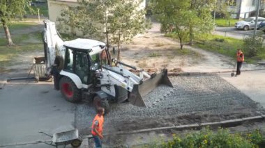 Yol çalışıyor. Kazıcı asfalt kaldırımını onarmak için ezilmiş taş döker, avluda derin bir çukur açar. İşçiler asfaltı asfaltlamadan önce küreklerle katman katman çalışırlar. Ukrayna, Kiev 5 Ekim 2020