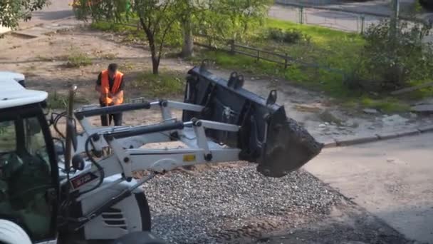 El camino funciona. Excavadora derrama piedra triturada para reparar pavimento de asfalto, agujero profundo en la carretera en el patio. Los trabajadores trabajan con palas para nivelar la capa antes de pavimentar el asfalto. Ucrania, Kiev octubre 5, 2020 — Vídeos de Stock