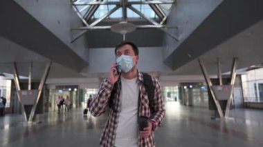 Koruyucu maske takan bir adam kahve içmek için kahve tutuyor, cep telefonuyla konuşuyor ve havaalanı terminaline gidiyor. İnsanlar Coronavirus salgını sırasında seyahat ederler. Yeni normal. Ukrayna, Kiev 10 Eylül 2020