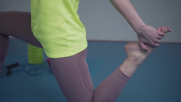 Ung sportig kvinna sträcker på benen innan träning på gym. Passformad träning som sträcker sig och värmer upp på golvet i fitnessstudion. Yogastudion. Vilar musklerna. Sportswoman hög kroppsflexibilitet — Stockvideo