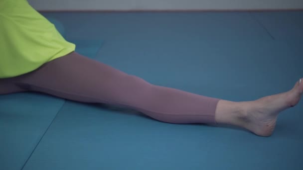 Junge, sportliche Frau, die vor dem Training im Fitnessstudio die Beine streckt. Fit-Kurs beim Dehnen und Aufwärmen auf dem Boden im Fitnessstudio. Yoga-Studio. Ruhige Muskeln. Sportlerin hohe Beweglichkeit des Körpers — Stockvideo