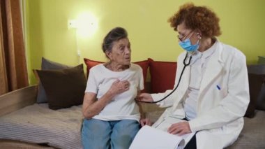 Steteskop tutan olgun bir kadın doktor evde yaşlı bir büyükanne hastayı muayene ediyor. Kadın hekim, huzurevinde yaşlı hastaların kalbini dinler. Sağlık hizmeti konsepti. Hekimler akciğerlere yardımcı oluyor.