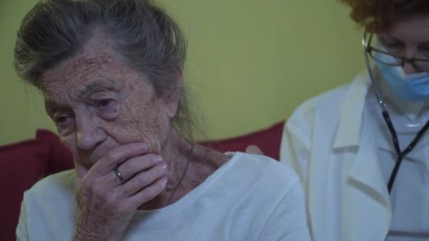 Mature woman doctor holding stethoscope examining senior grandma patient at home. Female physician listens to aged patients heart in a nursing home. Health care concept. Physician auscultating lungs — Stock Video