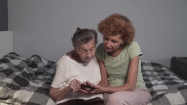 Olgun kız, huzurevinde yaşlı anneyi ziyaret eder ve akıllı telefon kullanmayı öğretir. Yaşlı gönüllü, yeni teknolojileri açıklıyor ve yaşlı kadının cep telefonuna baktığını gösteriyor.