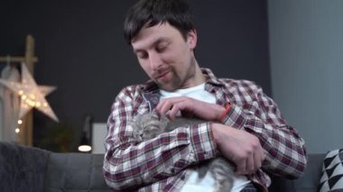 İskoç düz kulaklı gri kedi yavrusu ev sahibinin kollarında uyur. Safkan küçük sevimli İngiliz kedisi genç bir adamın ellerinde uyuyakalıyor. Erkek ve evcil hayvan teması. Erkek, uyuyan kedicik.