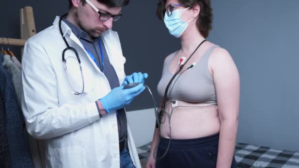 Mladý kavkazský lékař kardiolog provádí kardiologické vyšetření u pacientek se zdravotnickým prostředkem Holter monitorující EKG srdeční frekvenci. Test Holterova monitoru. Přenosný elektrokardiogram. ECG — Stock video