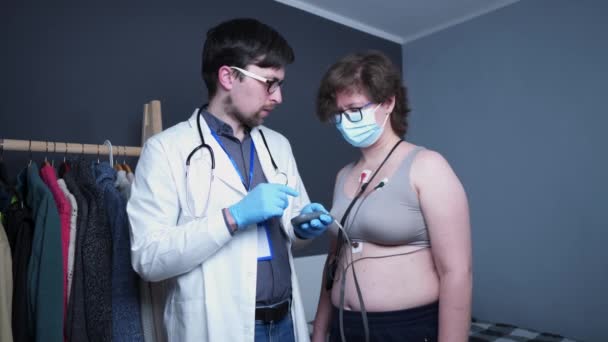 Jovem médico cardiologista caucasiano do sexo masculino fazer exame cardiológico para paciente mulher com dispositivo médico holter monitoramento ecg frequência cardíaca. Teste do monitor Holter. Eletrocardiograma portátil. ECG — Vídeo de Stock