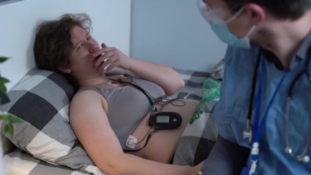 Covid 19, koronavirüs. Doktor karantina sırasında eve geliyor, hasta kadın oksijen maskesiyle yatakta yatıyor, sağlık görevlisi kalp fonksiyonlarını kontrol ediyor. İlk yardım, ilk yardım. — Stok video