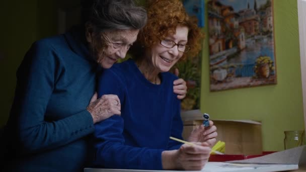 Senior par 90 år gammal mamma och äldre dotter kram och målning. Pensionering, lära sig nya hobby måla bilder med borste tillsammans hemma i karantän. Att tillbringa lycklig tid med ensamstående mor — Stockvideo